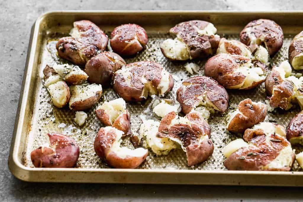 Par-boiled baby red potatoes on a baking tray, smashed down.