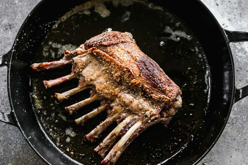 A rack of lamb chops searing in a cast iron pot.