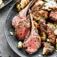 Three rib-in lamb chops on a plate with roasted rosemary potatoes.