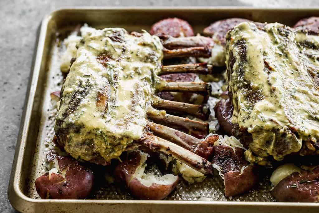Lamb racks with garlic herb topping, on top of smashed red potatoes on a baking tray.