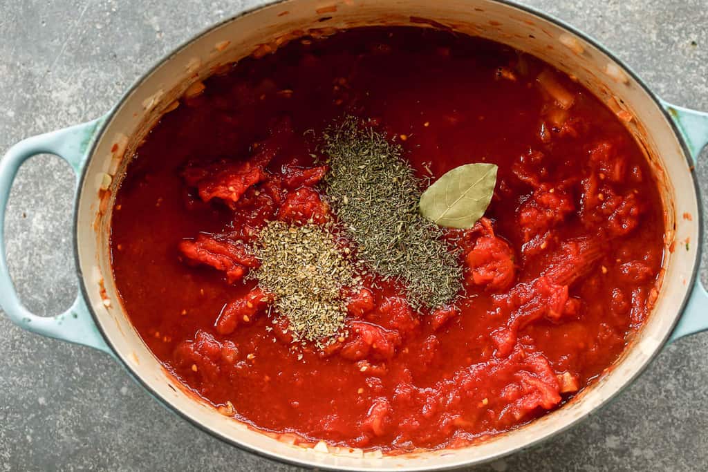 Tomates broyées, épices et feuille de laurier ajoutées à une marmite avec des légumes sautés, pour faire du bouillon pour cioppino.