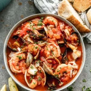 Cioppino served in a bowl, with lemon wedges and sourdough bread slices on the side.