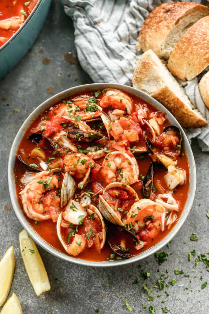 Cioppino served in a bowl, with lemon wedges and sourdough bread slices on the side.