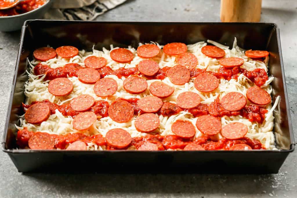 Pepperoni slices added on top of Detroit pizza, ready to bake.