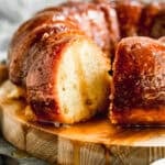 An easy Rum Cake recipe served on a wooden platter with a glaze drizzled on top and a piece cut to show the soft texture.