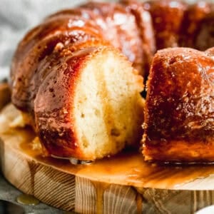An easy Rum Cake recipe served on a wooden platter with a glaze drizzled on top and a piece cut to show the soft texture.