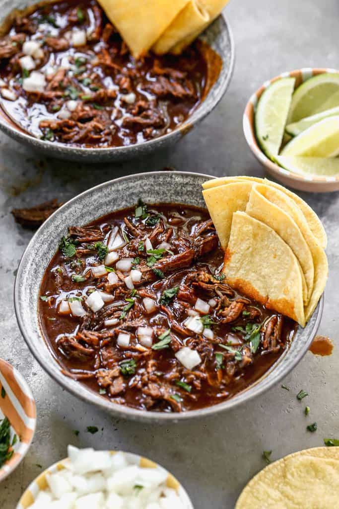 Beef Birria served in a bowl, garnished with cilantro and onion, and served with corn tortillas.