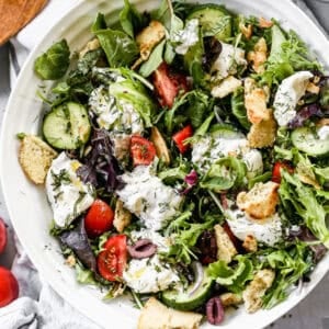 A tomato Burrata Salad recipe with a simple lemon vinaigrette, veggies, fresh herbs, and toasted pita croutons.