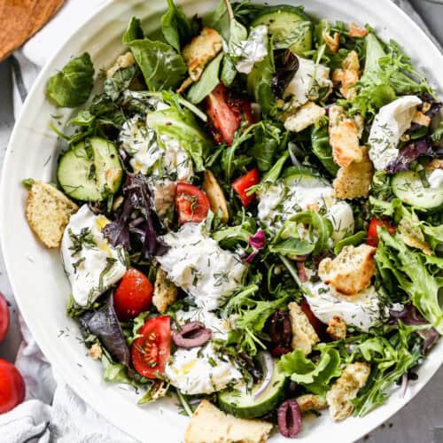 A tomato Burrata Salad recipe with a simple lemon vinaigrette, veggies, fresh herbs, and toasted pita croutons.
