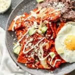 A homemade Chilaquiles recipe tossed in a delicious sauce with queso fresco and Mexican crema sprinkled on top and served with black refried beans and a fried egg.