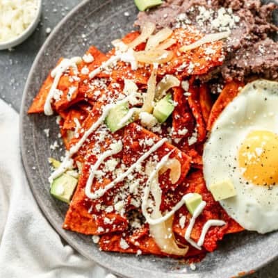 A homemade Chilaquiles recipe tossed in a delicious sauce with queso fresco and Mexican crema sprinkled on top and served with black refried beans and a fried egg.
