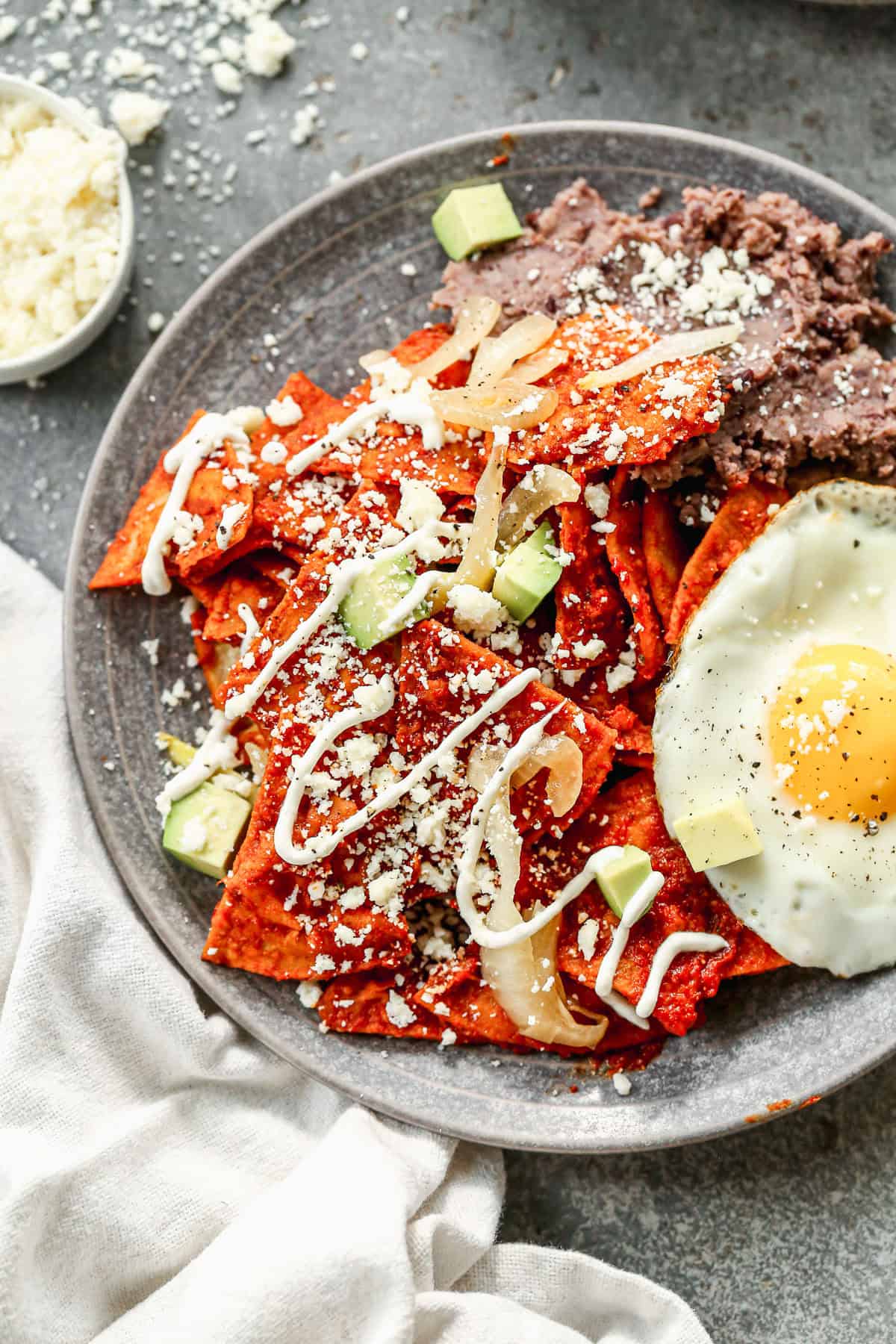 A homemade Chilaquiles recipe tossed in a delicious sauce with queso fresco and Mexican crema sprinkled on top and served with black refried beans and a fried egg.
