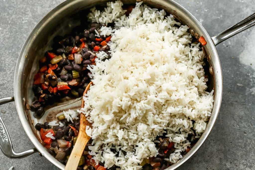 Restes de riz froids ajoutés à une poêle avec des haricots noirs et des légumes sautés.