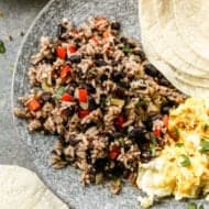 Gallo pinto served on a plate with some scrambled eggs and a tortilla on the side.