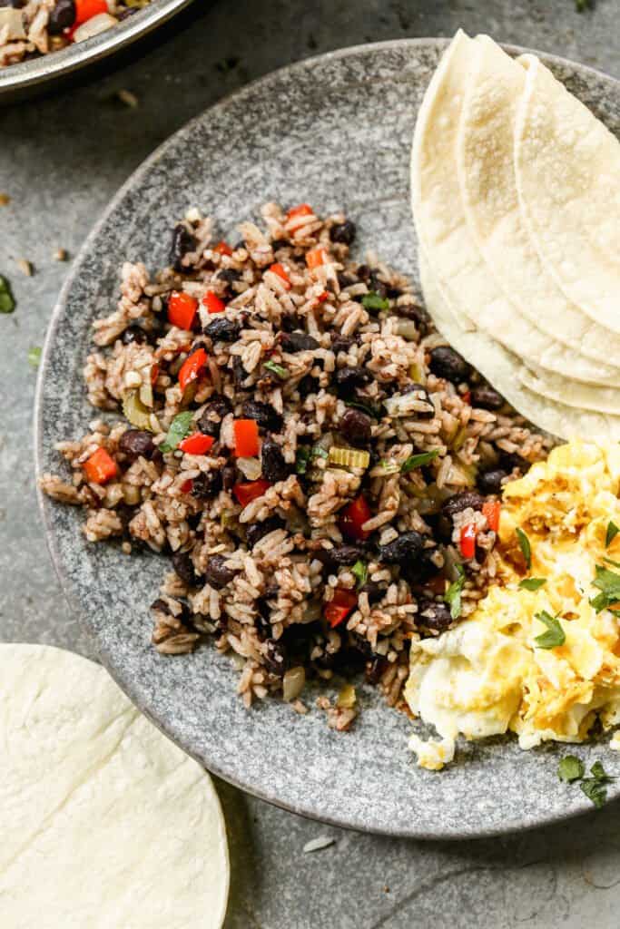 Gallo pinto served on a plate with some scrambled eggs and a tortilla on the side.