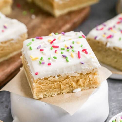 A frosted Sugar Cookie Bar on a square of parchment paper, topped with rainbow sprinkles.