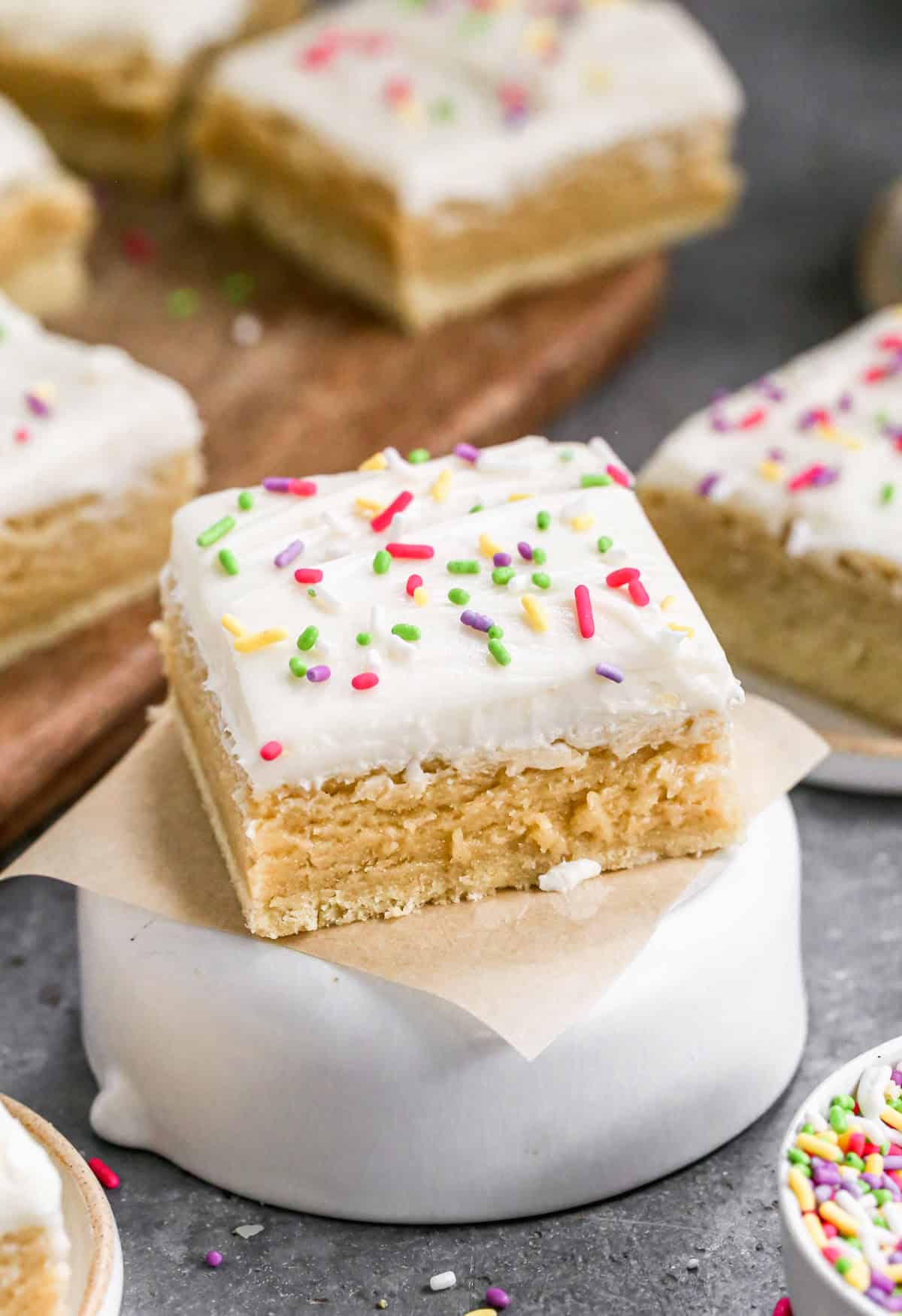 A frosted Sugar Cookie Bar on a square of parchment paper, topped with rainbow sprinkles.