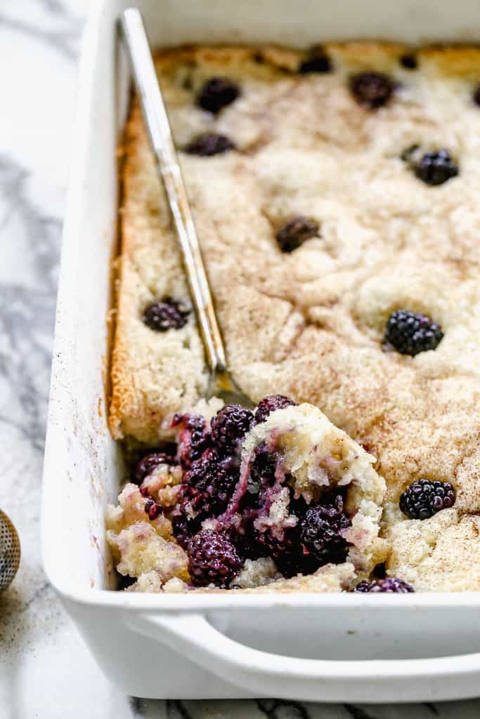 A piece of fresh Blackberry Cobbler being lifted from the pan with a spoon.