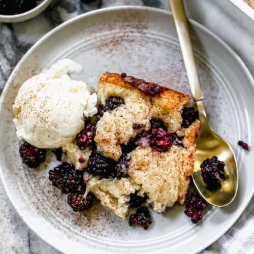 A piece of homemade Blackberry Cobbler on a plate with a scoop of vanilla ice cream and a spoon.