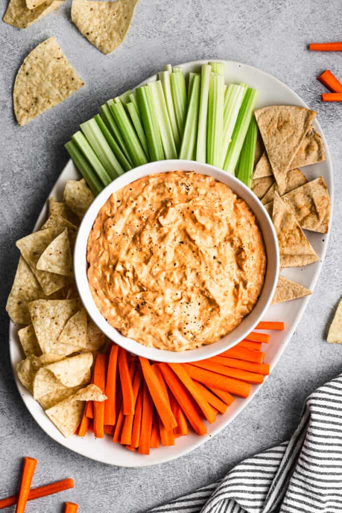 An easy Buffalo Chicken recipe in a white bowl surrounded by chips, celery, and carrots.