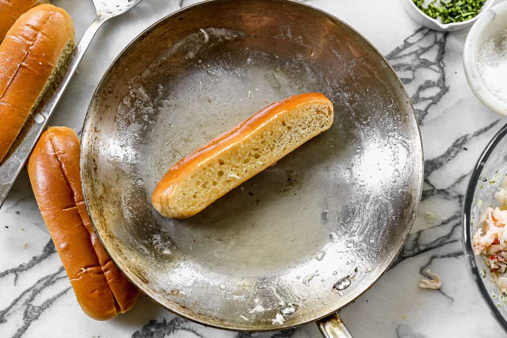 A pan with a sandwich roll being toasted in butter for lobster rolls.