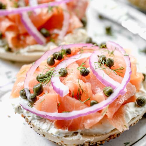 A lox bagel with cream cheese, smoked salmon, red onion, capers, and fresh dill on a plate.