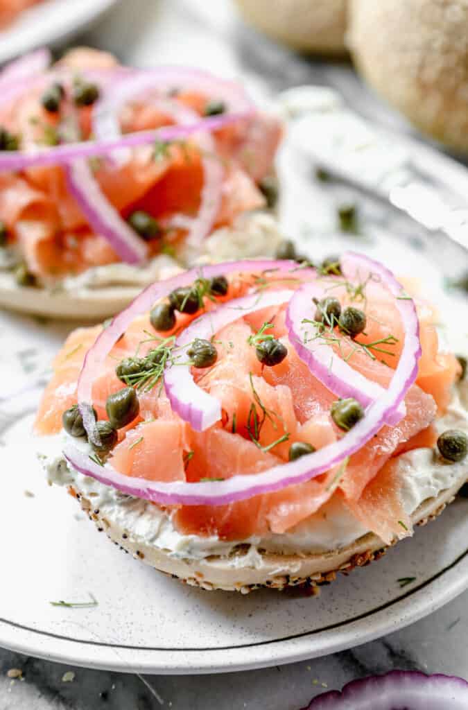 A lox bagel with cream cheese, smoked salmon, red onion, capers, and fresh dill on a plate.