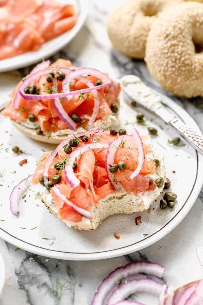 Two lox bagels served on a plate, topped with cream cheese, salmon, capers, dill and onion.