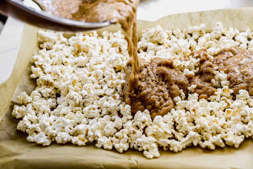 Caramello caldo fresco che viene versato su un popcorn su una teglia, pronto per essere cotto per i migliori popcorn al caramello.