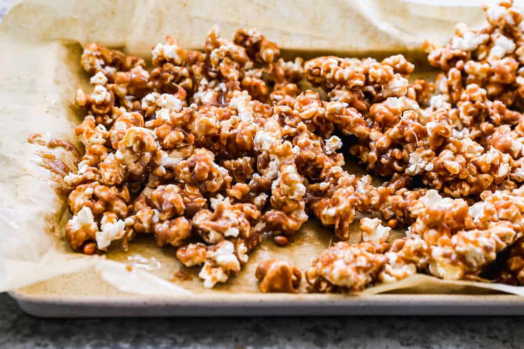 Baked Caramel Popcorn on a brown parchment paper lined baking sheet. 