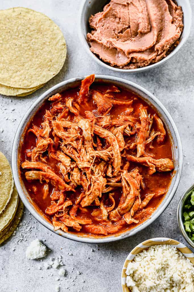 Chicken Tinga served in a bowl, with tortillas, beans and other toppings on the side.