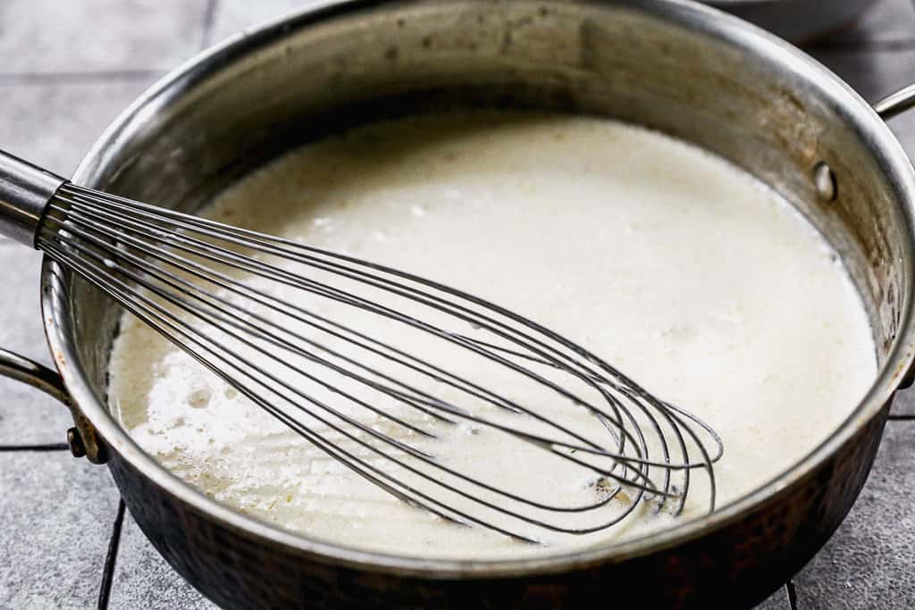 A pan with homemade alfredo sauce and a whisk.