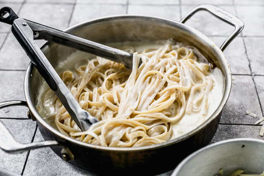 A pan with fresh easy Fettuccine Alfredo and tongs, ready to serve. 
