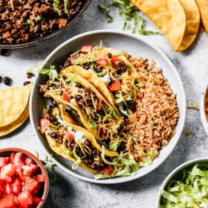 Three of the BEST Ground Beef Tacos with crispy shells and toppings on a plate with Mexican Rice.