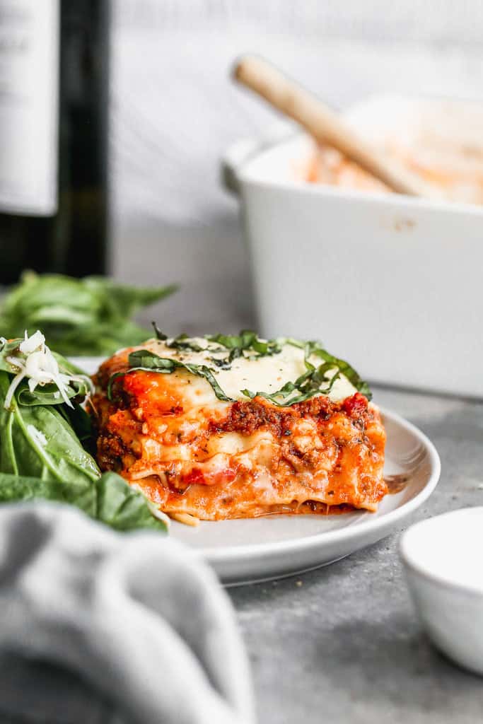 A slice of Homemade Lasagna on a white plate with a green salad.