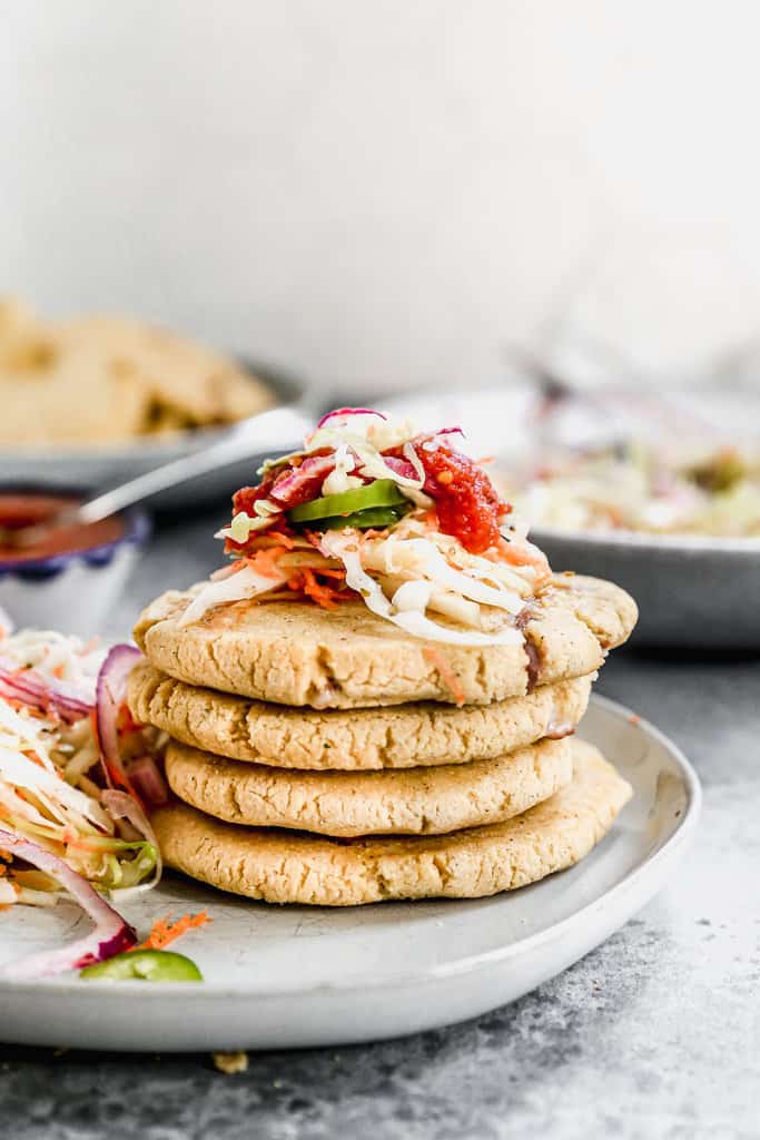 A stack of 4 homemade Pupusas on a plate with Curtido and Salsa Roja on top.