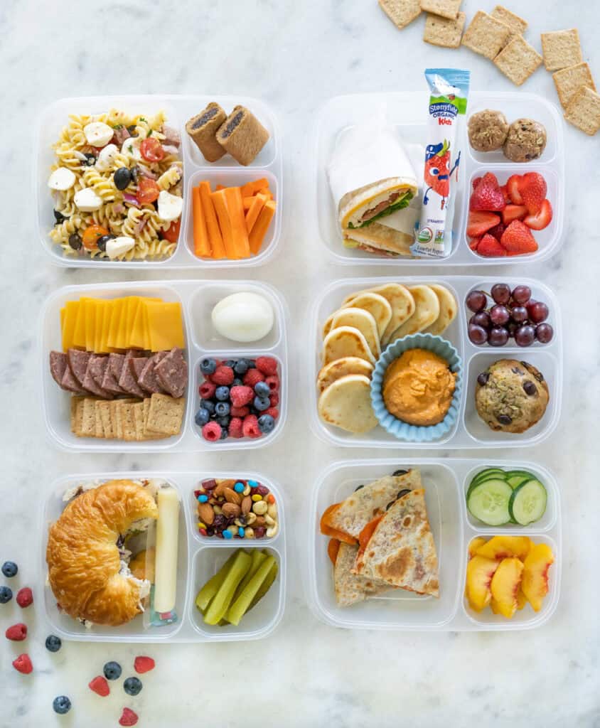 Six school lunches packed and in containers with compartments, showcasing a variety of healthy lunches to pack your child for school lunch.