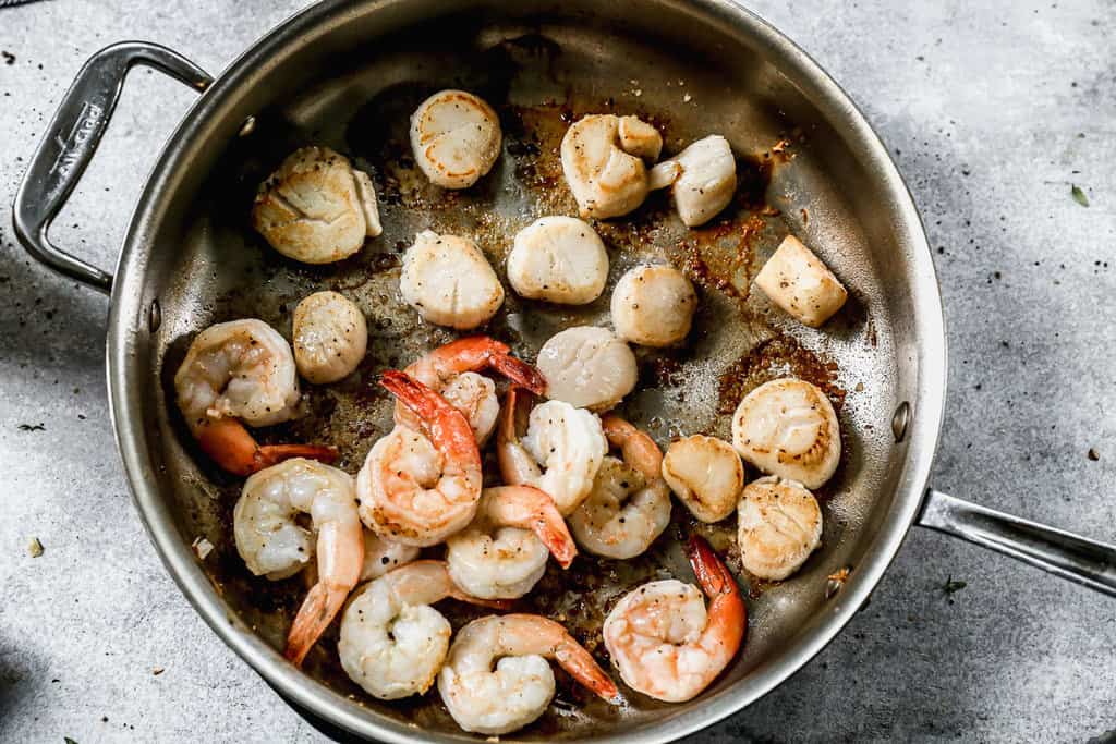 Shrimp and scallops being cooked in a pan to make seafood pasta.
