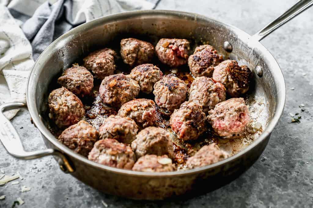 Homemade meatballs being browned in a pan for Swedish Meatballs.
