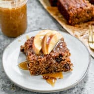 A piece of Apple Spice Cake on a plate and topped with fresh apples and a drizzle of homemade caramel sauce.