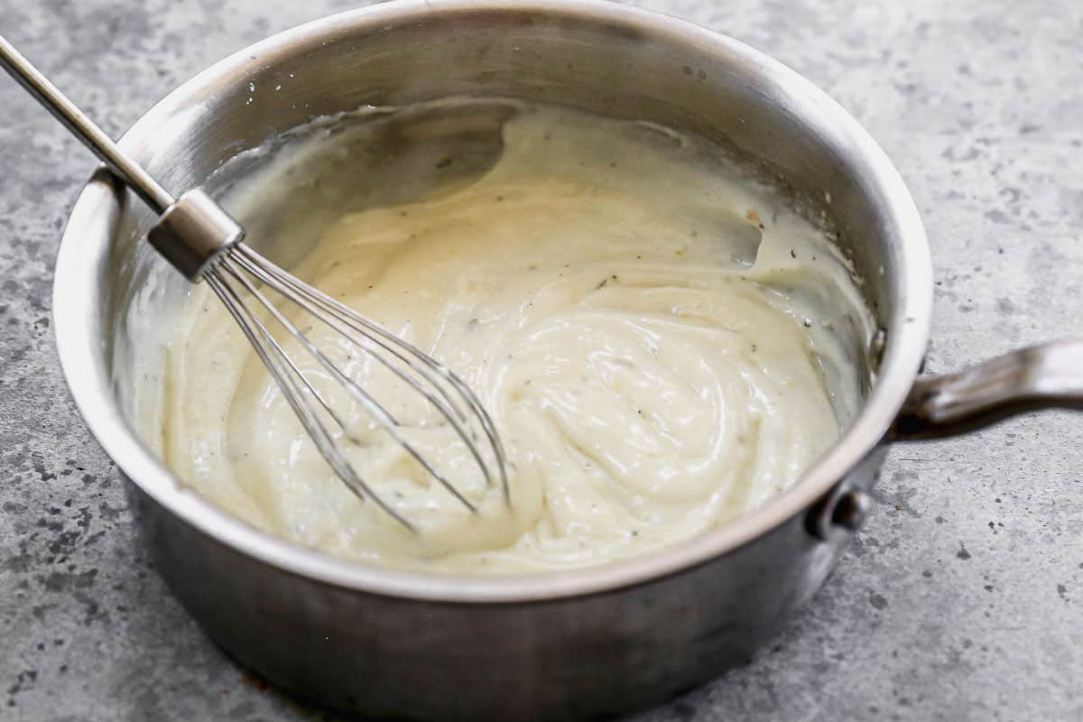 Homemade Cream of Chicken Soup Substitute in a stainless steel saucepan with a whisk.