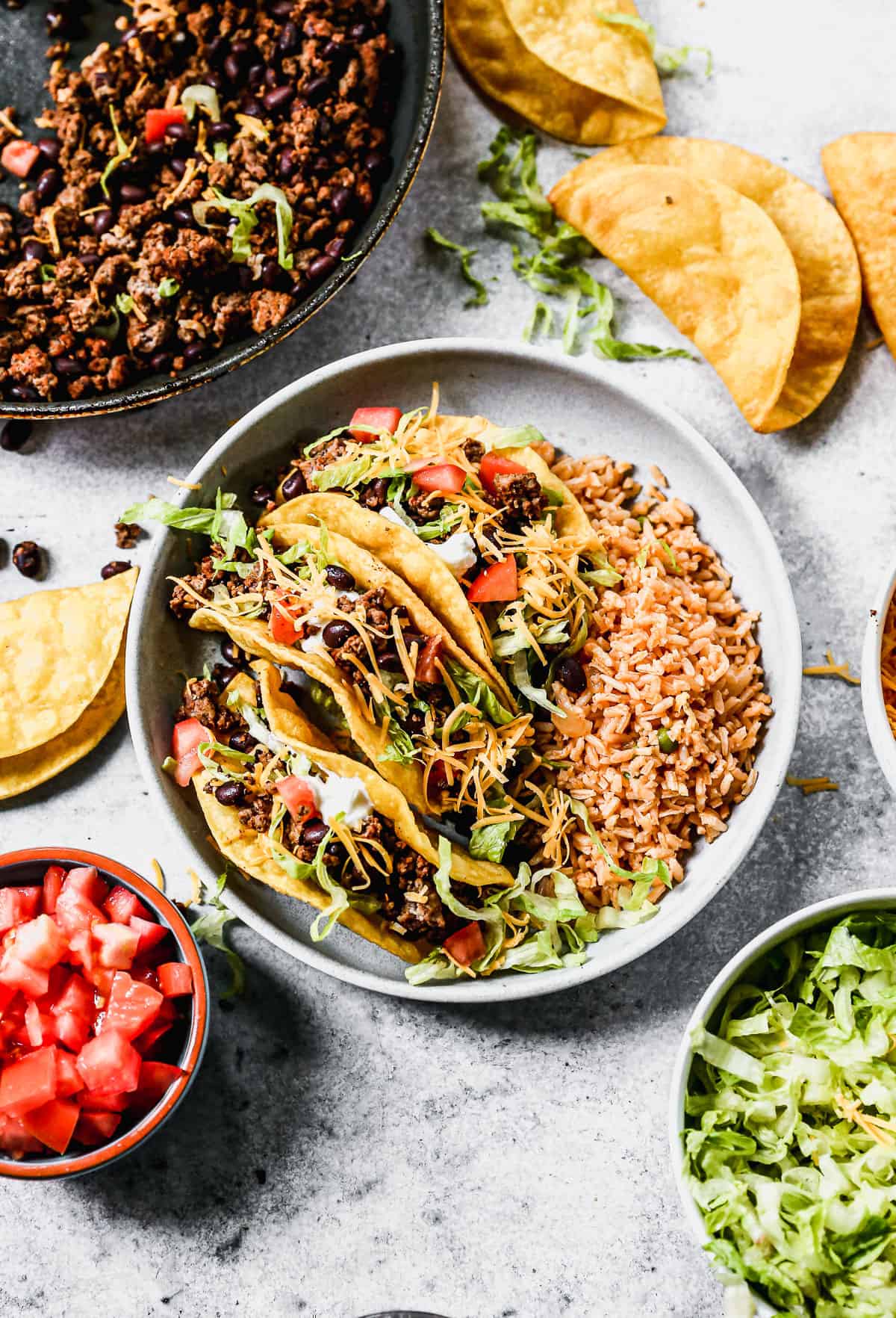 Three ground beef tacos with crispy shells and toppings on a plate with Mexican rice.