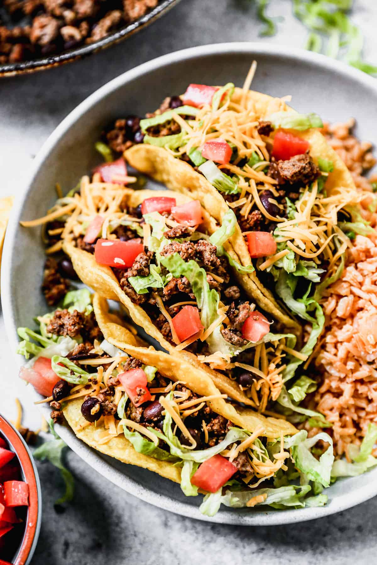 Gambar close-up dari tiga Taco Daging Sapi giling terbaik dengan topping di atas piring dengan nasi Meksiko.