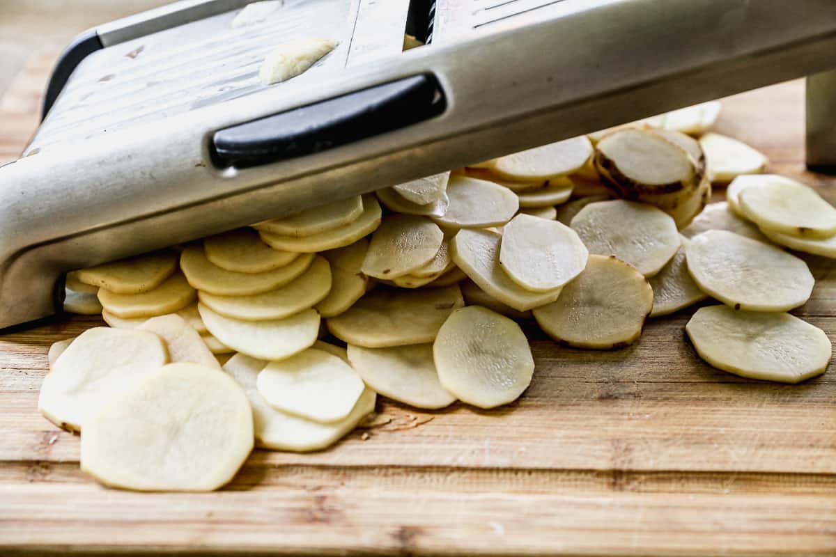 Alat pengiris mandolin dengan tumpukan irisan kentang untuk membuat Potatoes Au Gratin.