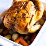 A golden Roast Chicken fresh from the oven on top of carrots and potatoes.