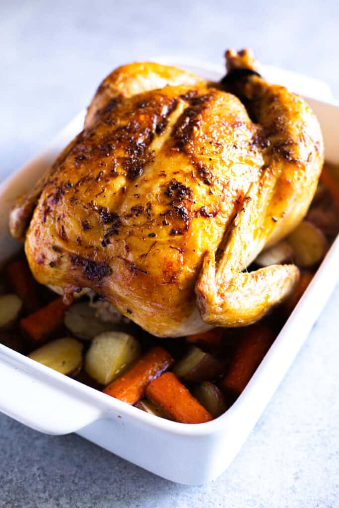 A golden Roast Chicken fresh from the oven on top of carrots and potatoes.