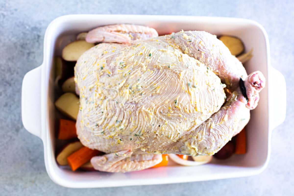 A raw chicken covered in herb butter on top of vegetables, ready to bake. 