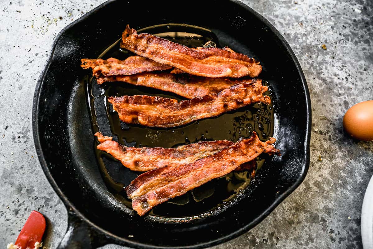 Panci besi cor dengan bacon panas dan renyah untuk membuat Shrimp and Grits.