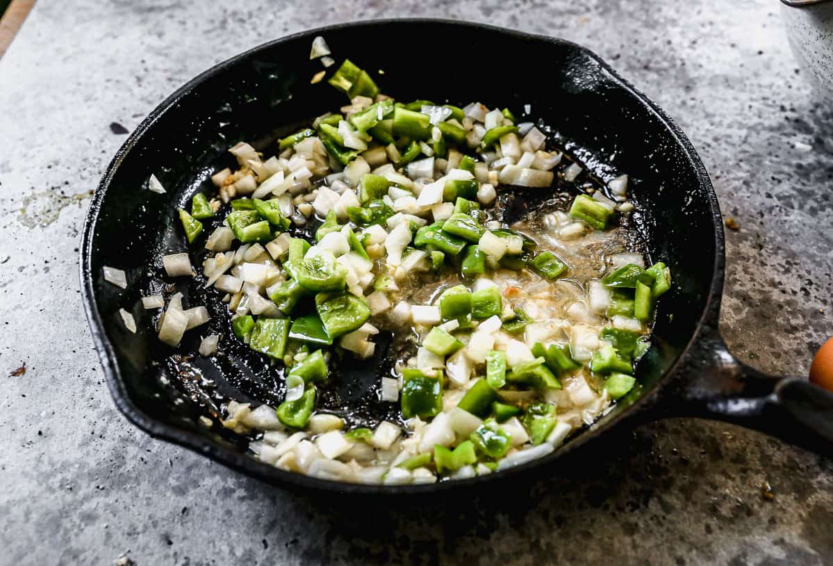 A cast iron pan with diced onion and green pepper being sautéed in butter. 