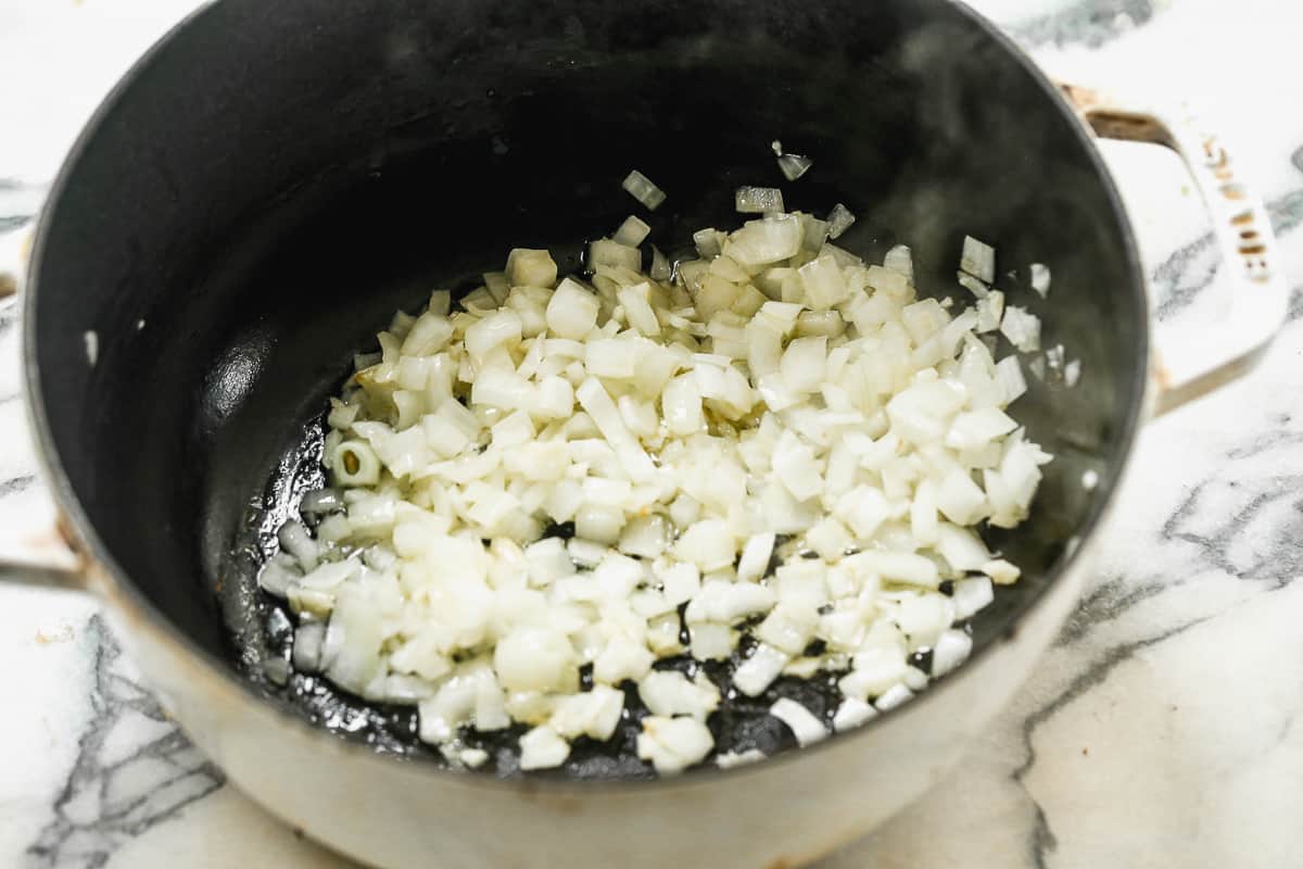Diced onion being sautéed in olive oil in a large pot.